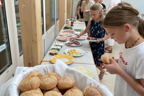 Ein Buffet mit verschiedenen Speisen in einer hellen Umgebung, während Kinder und Erwachsene essen und sich bedienen.